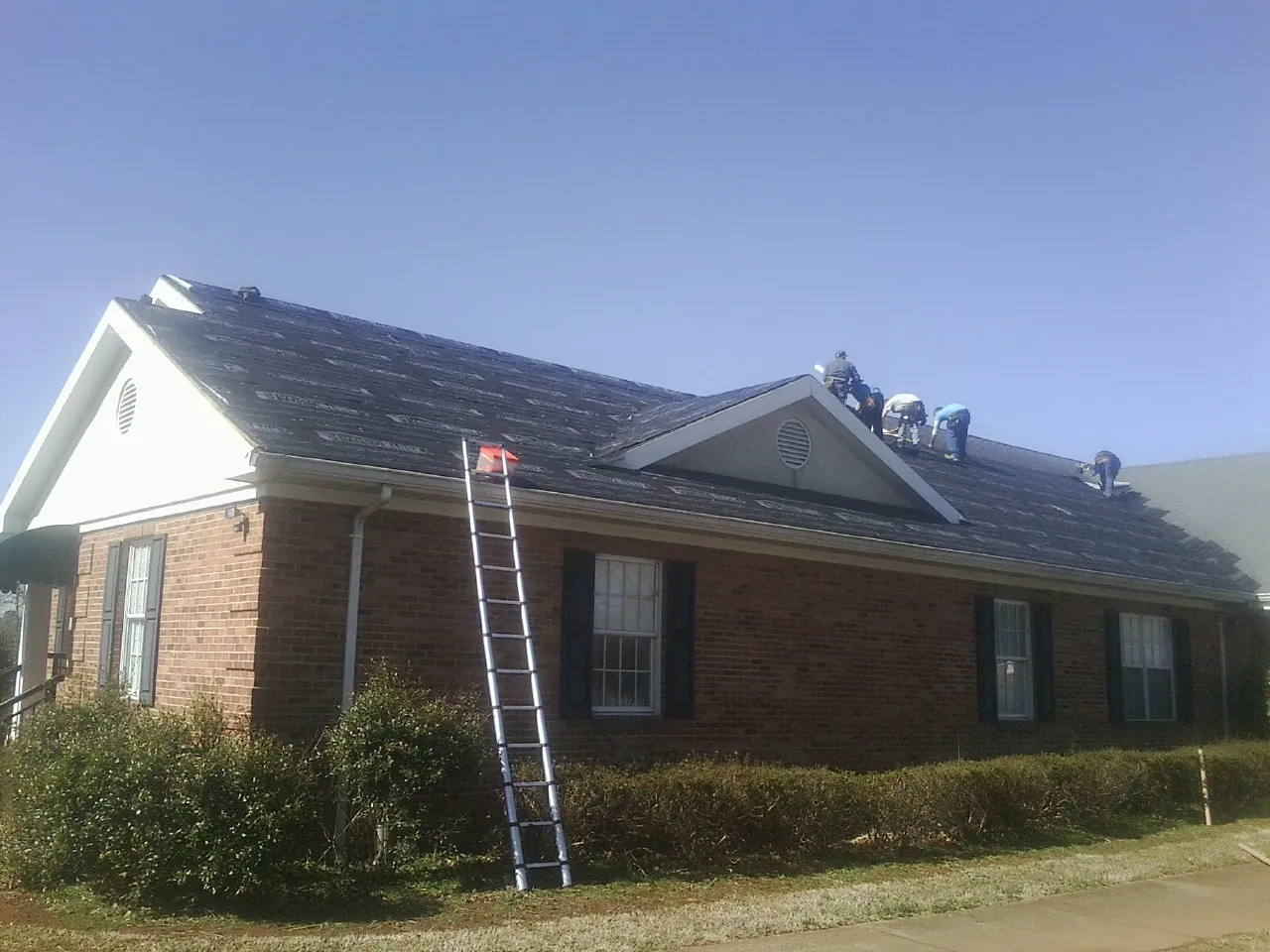Crew tearing shingles off a brick ranch roof with a ladder set — Metal Roof Repair work by our crew in Canterbury