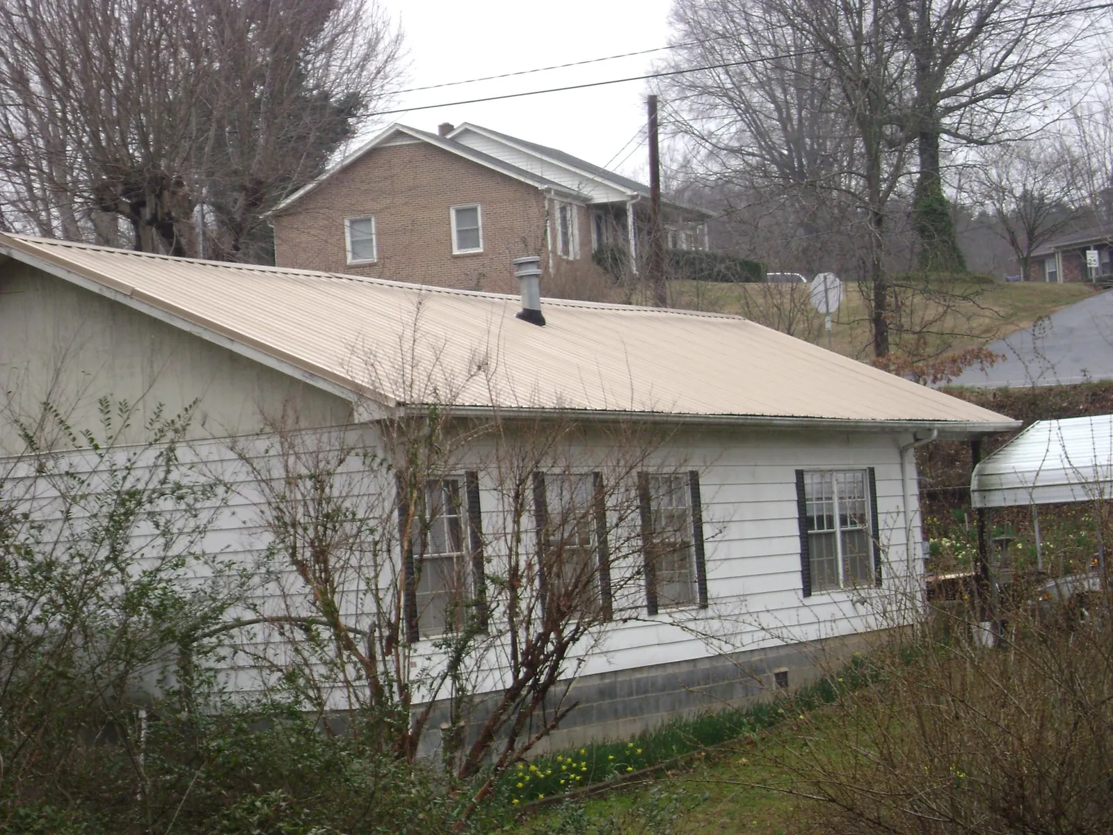 Tan metal roof on a white sided house set into a hillside — Commercial Roofing by Roofing Brothers in Canterbury